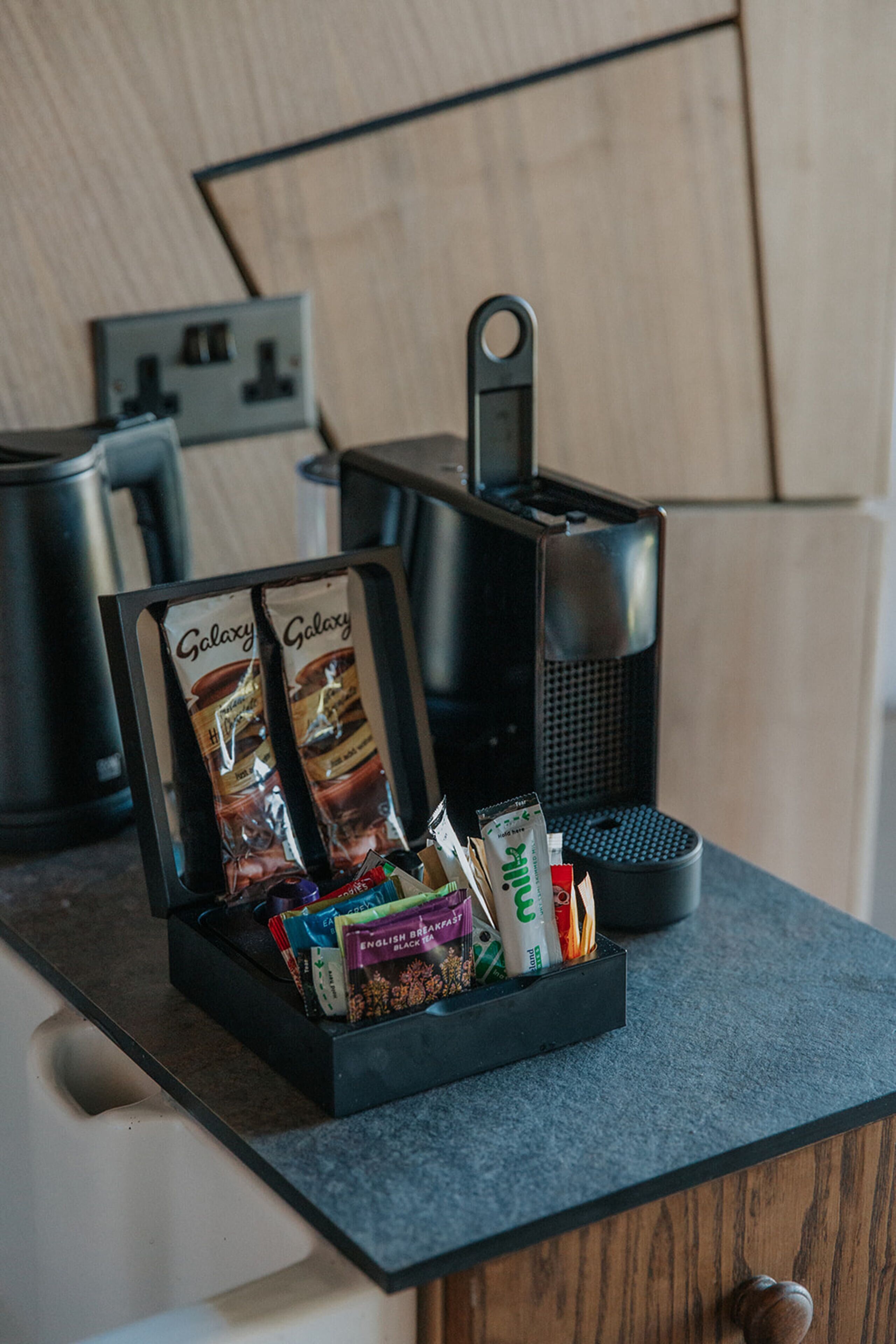 Un coin cuisine équipé d’une machine à café, d’un plateau noir contenant des capsules de café et d’un menu encadré.