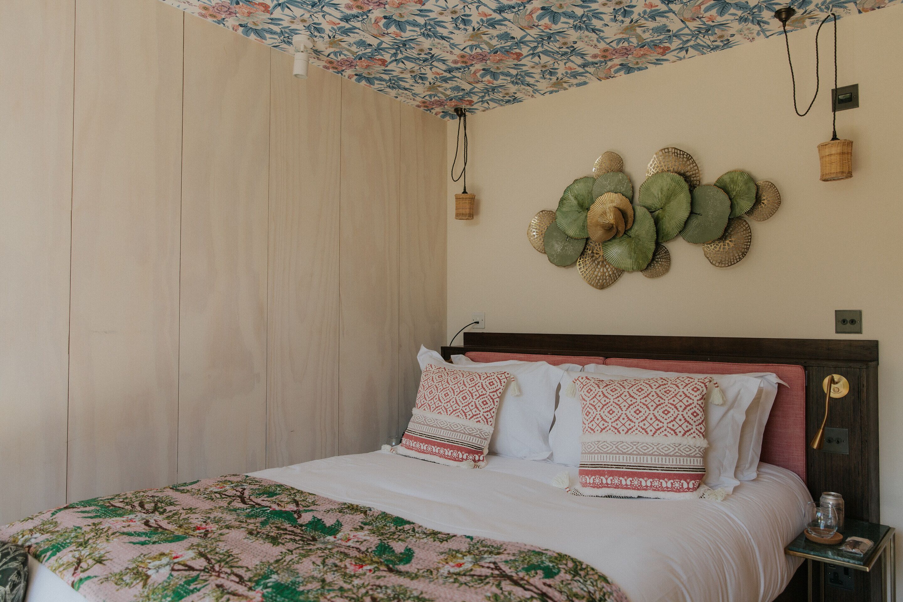 A neatly made bed with patterned bedding, a wooden headboard, and a floral ceiling design.