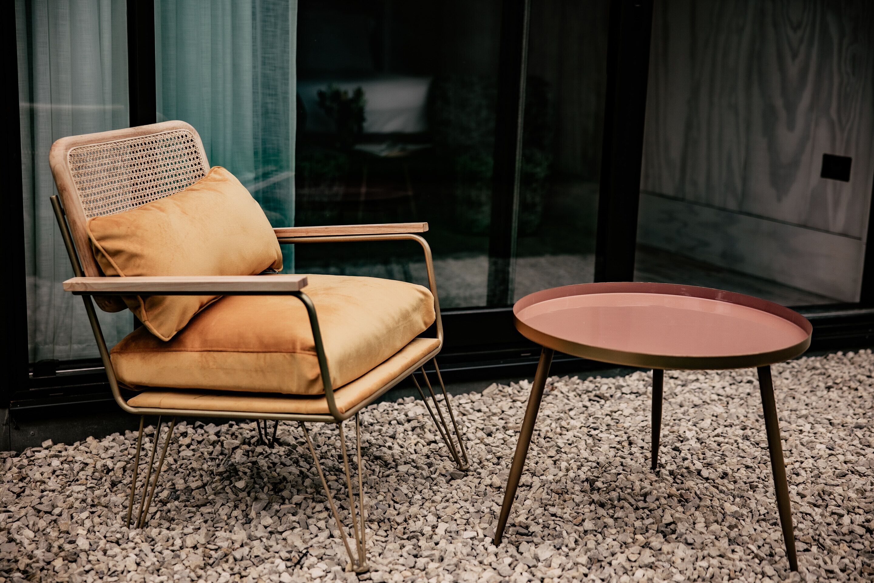 A modern room with a wicker chair and a small round table on a gravel floor.