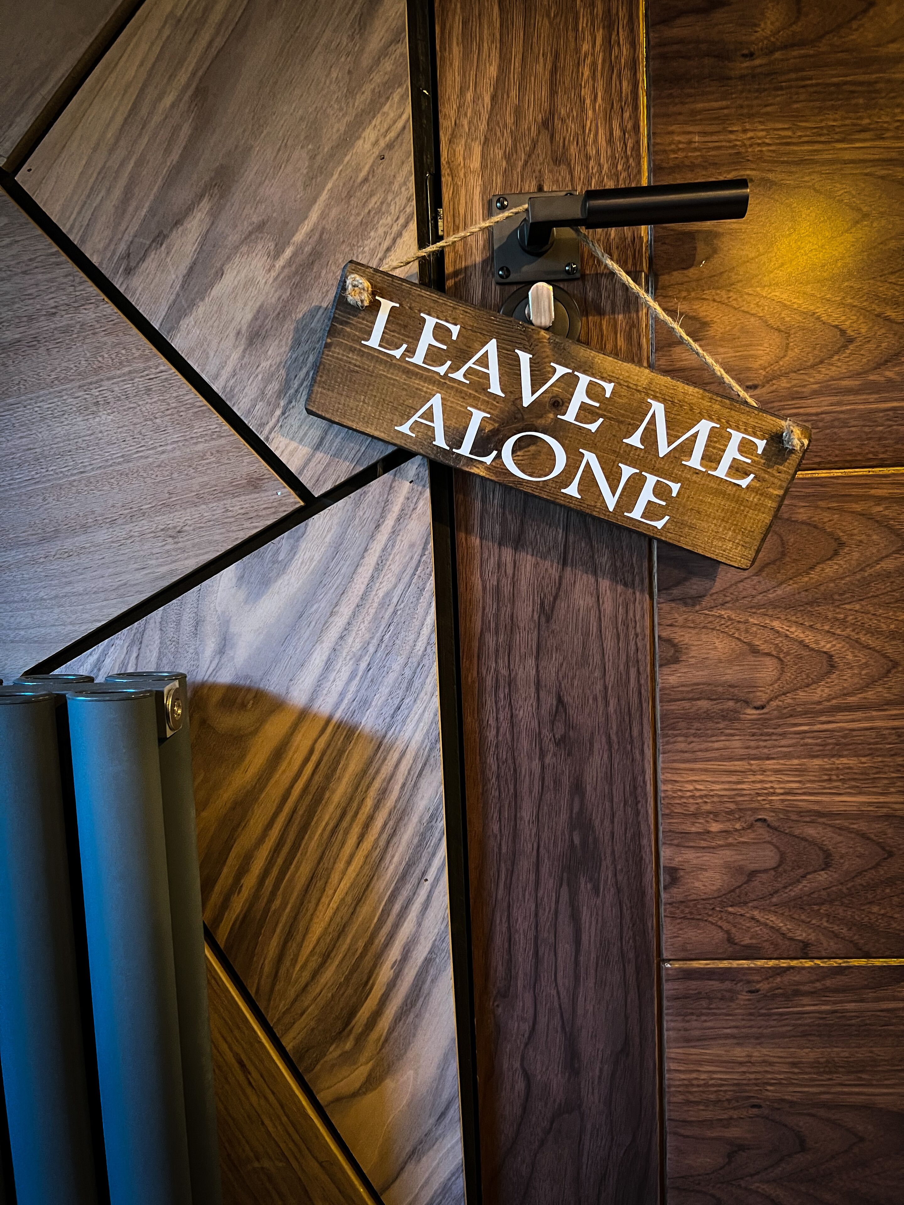 A wooden door with a sign that reads "LEAVE ME ALONE" hanging on it.