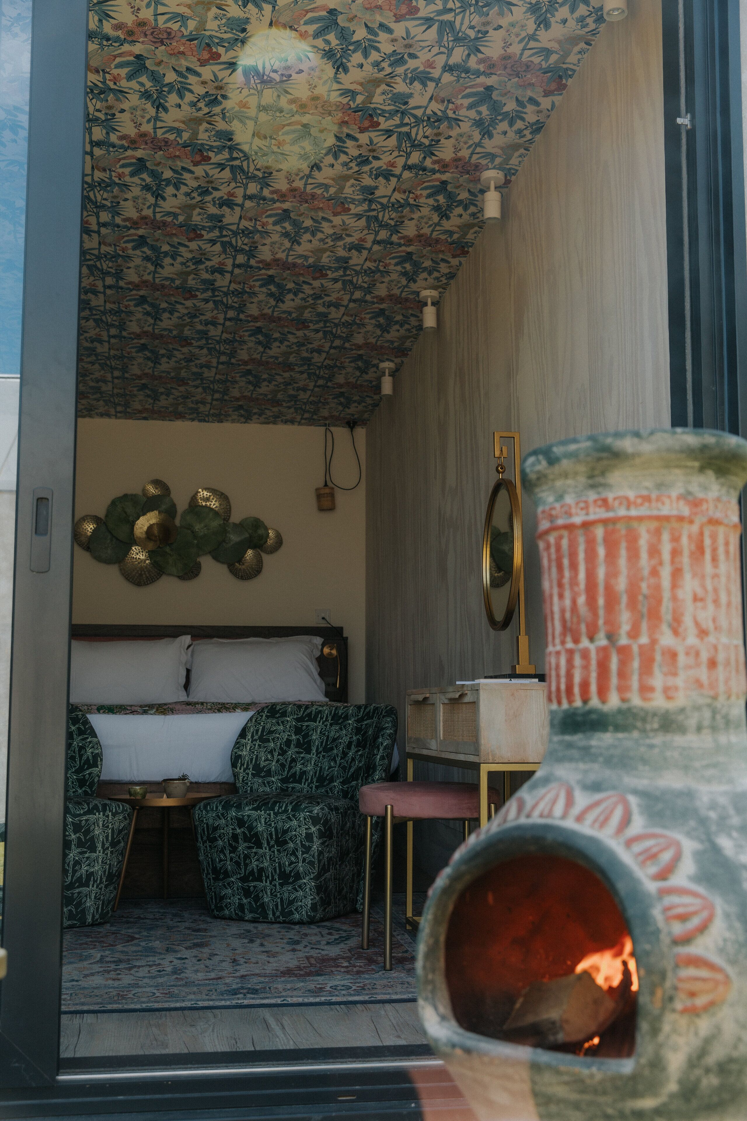 Ein Zimmer mit einem Bett, einem Sessel, einem kleinen Tisch und einer dekorativen Vase mit einer Flamme.