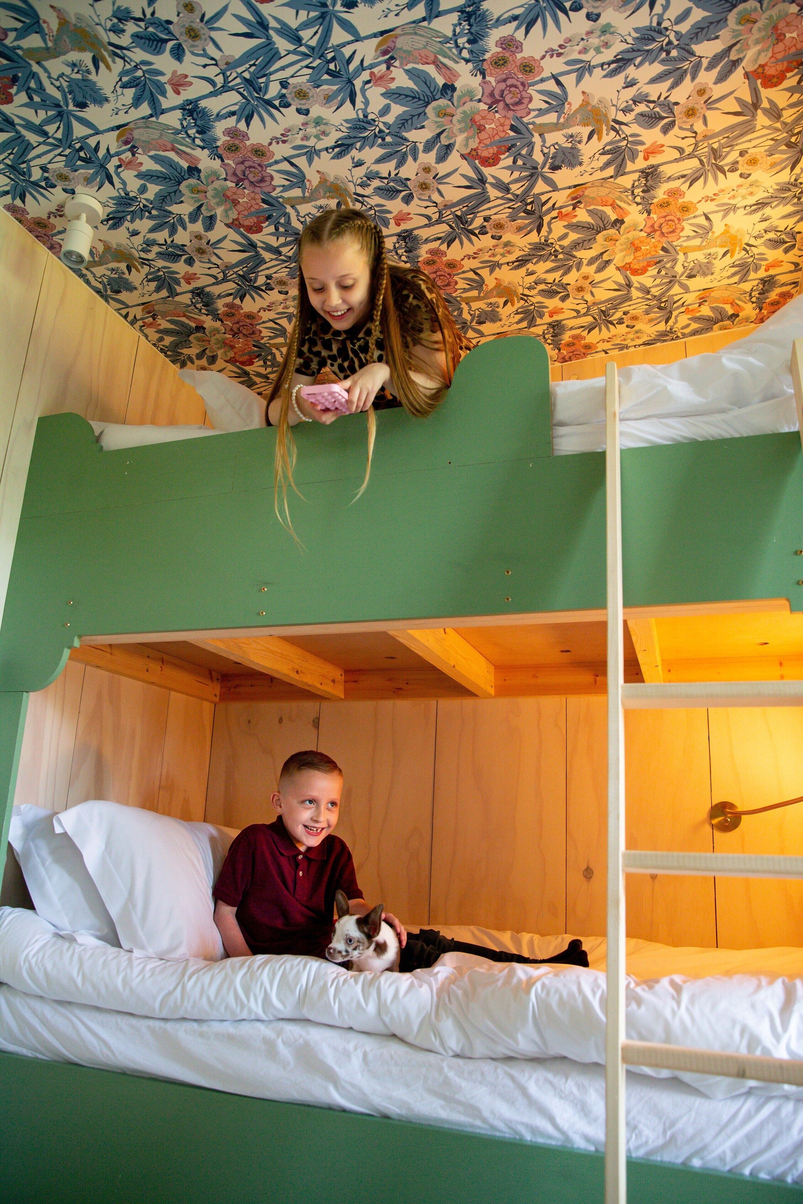 A bunk bed room with a floral wallpaper, a wooden ceiling, and a green wall.