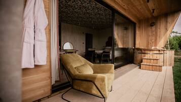 A wooden interior with a beige armchair, a wooden bench, and a glass door leading to an outdoor area.