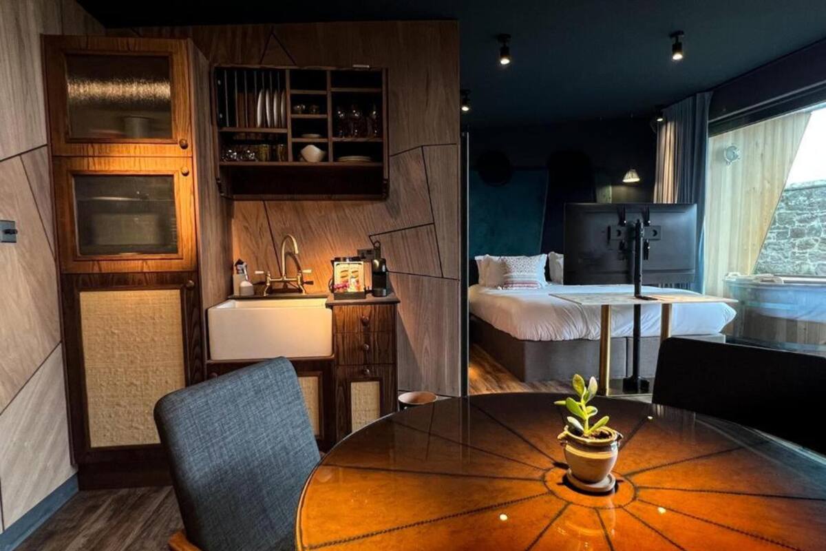 Una habitación de hotel moderna con un armario de madera, un lavamanos, una cama, una mesa con una planta y una ventana con vistas.