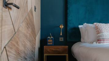 A bedroom with a wooden wardrobe, a bedside table with a lamp, and a bed with a blue headboard.
