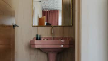 A bathroom with a wooden door, a pink sink, and a mirror with a gold frame.