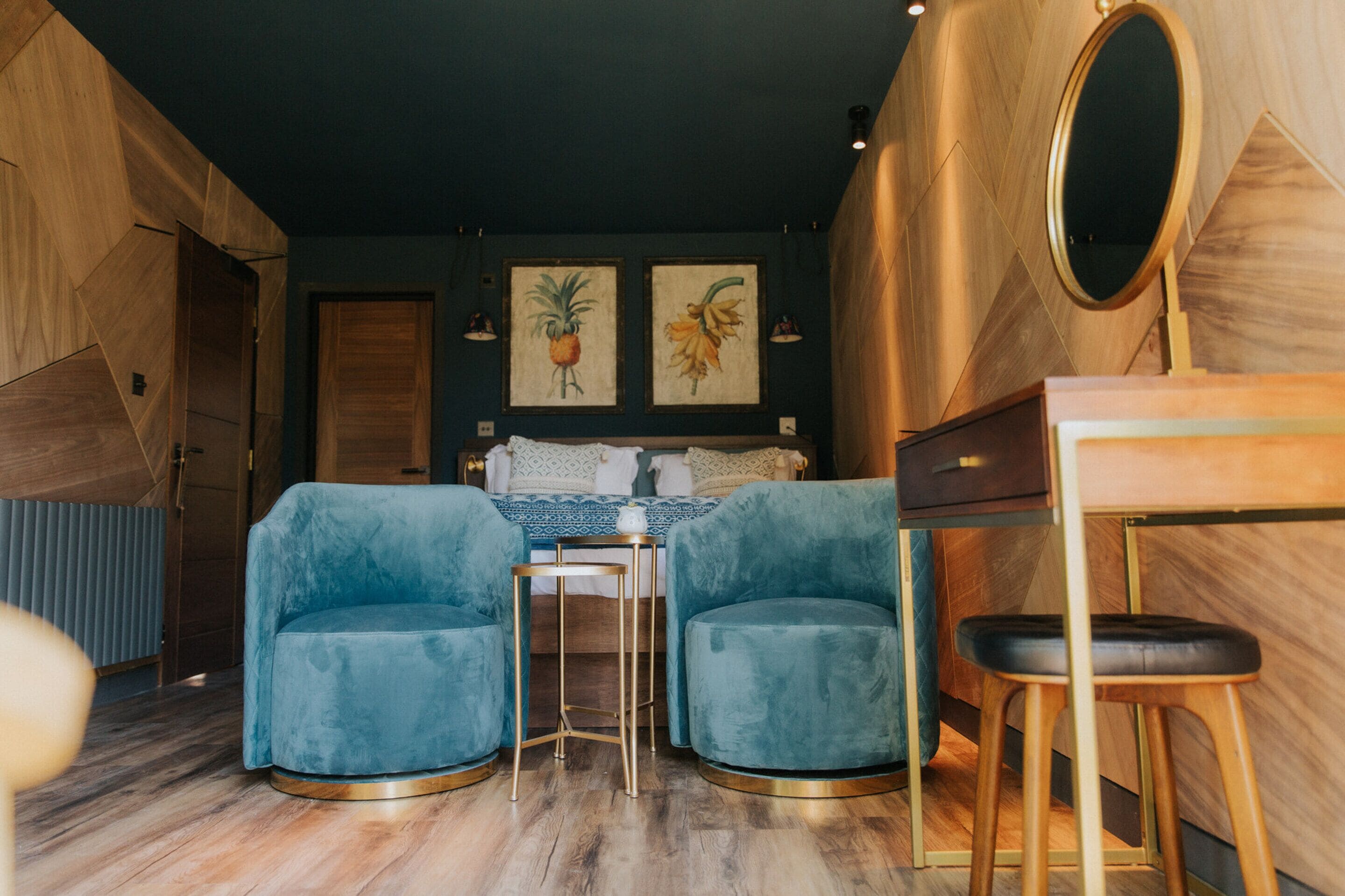 Una habitación moderna con una cama, dos sillones azules, una mesita y un espejo.