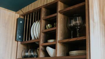 A wooden cabinet with shelves containing plates, bowls, and wine glasses.