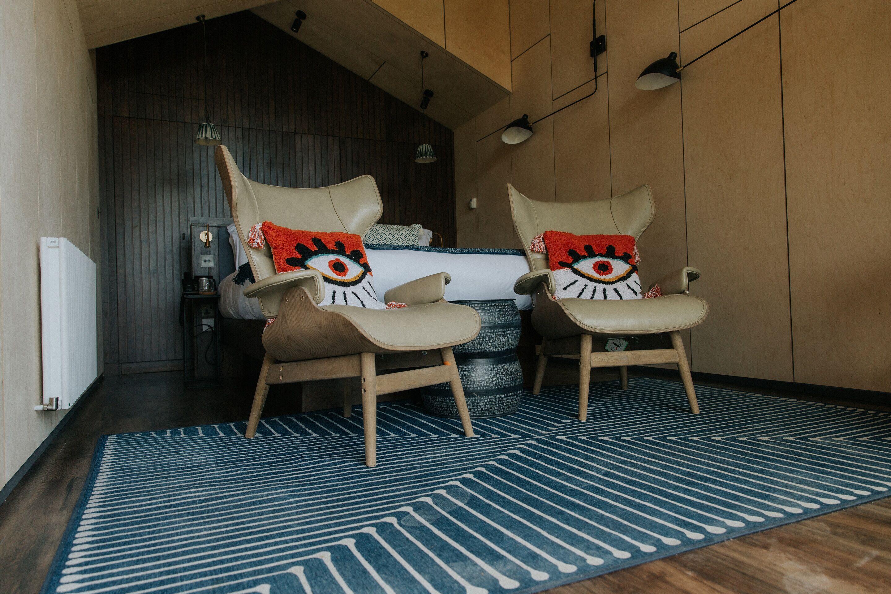 Een moderne kamer met twee stoelen, een bed en een blauw kamerkleed.