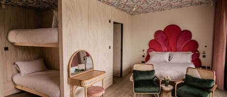 A room with a bunk bed, a desk with a mirror, two green armchairs, and a red decorative headboard.