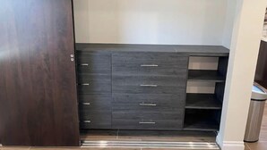 A walk-in closet with dark wood cabinets, a hanging rod, and a trash bin.