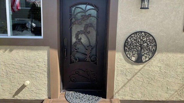 A brown door with intricate metalwork, a small circular metal tree decoration on the wall, and a window with a red and white striped towel hanging.