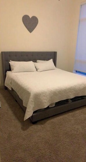 Cozy bedroom with a single bed, grey headboard, and white bedding, featuring a heart-shaped decoration above.
