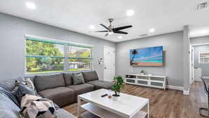 A modern living room with a grey sofa, a white coffee table, and a TV mounted on the wall. - Renovated 3BR, Fenced Yard, Brandon | Sleeps 8, 20 Min to Tampa, Monthly OK (Brandon)
