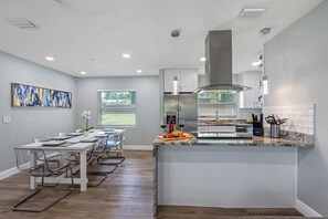 A modern kitchen with a marble countertop, stainless steel appliances, and a dining area with clear chairs and a white table.