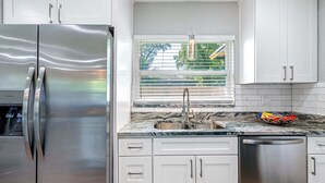A modern kitchen with stainless steel appliances, a granite countertop, and a window with blinds. - Renovated 3BR, Fenced Yard, Brandon | Sleeps 8, 20 Min to Tampa, Monthly OK (Brandon)