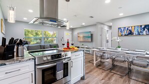 A modern kitchen with stainless steel appliances, a dining area with a glass table, and a large window providing a view of the outdoors. - Renovated 3BR, Fenced Yard, Brandon | Sleeps 8, 20 Min to Tampa, Monthly OK (Brandon)