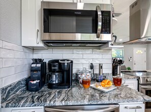 Una cocina con microondas integrado, cafetera y una encimera con una taza de té y un pastel.