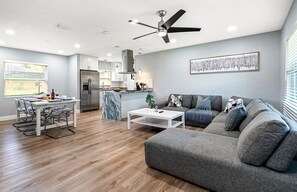 Ein modernes Wohnzimmer mit einem grauen Sofa, einem weißen Couchtisch und einem Essbereich mit Tisch und Stühlen.