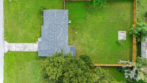 A residential property with a paved driveway, a lawn, a fenced garden area, and a house with a sloped roof. - Renovated 3BR, Fenced Yard, Brandon | Sleeps 8, 20 Min to Tampa, Monthly OK (Brandon)