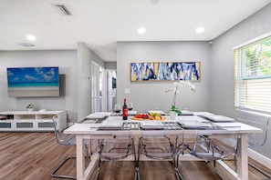 A modern dining area with a table set for two, a painting on the wall, and a television above the table.