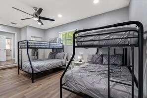 Ein Zimmer mit zwei Etagenbetten, einem Deckenventilator, einem Fenster mit Jalousien und einem Nachttisch mit Lampe.