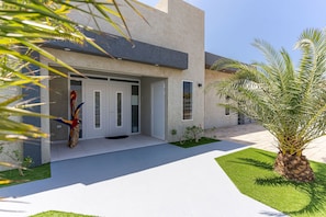 Una casa moderna con fachada blanca, puerta principal y un pequeño jardín con una palmera.