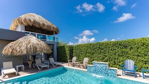 Une piscine dotée de chaises longues et d’une structure recouverte d’un toit de chaume.