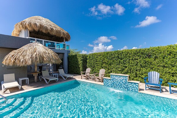 A swimming pool with lounge chairs and a thatched roof structure.