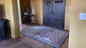 Un couloir doté d’un plancher en bois, d’un tapis à motifs, d’une porte en bois foncé et d’une petite table sur laquelle se trouvent un vase et un ordinateur portable.