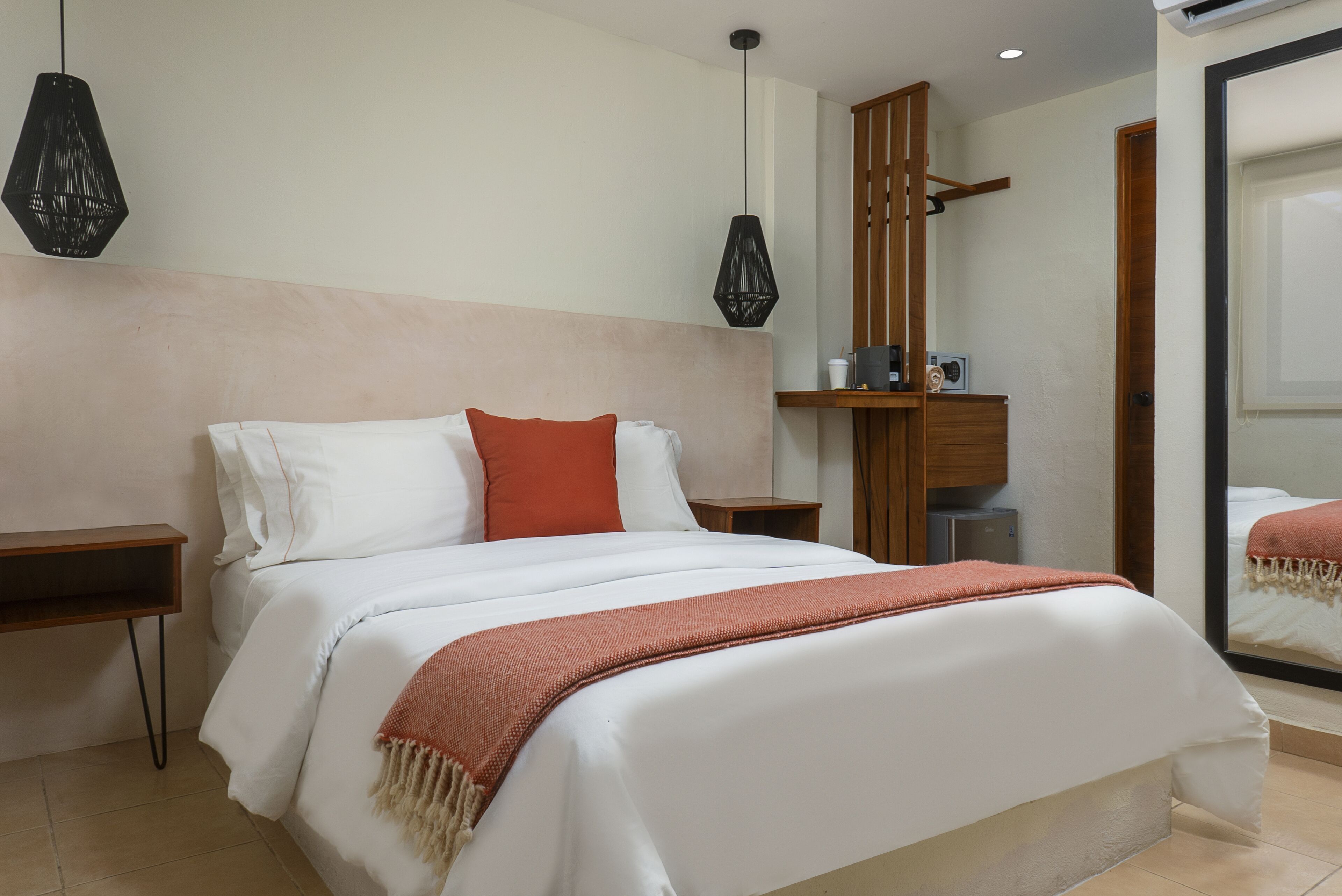 Uma cama bem arrumada com roupa de cama branca e vermelha, uma cabeceira de madeira e uma pequena mesa de cabeceira com uma luminária.