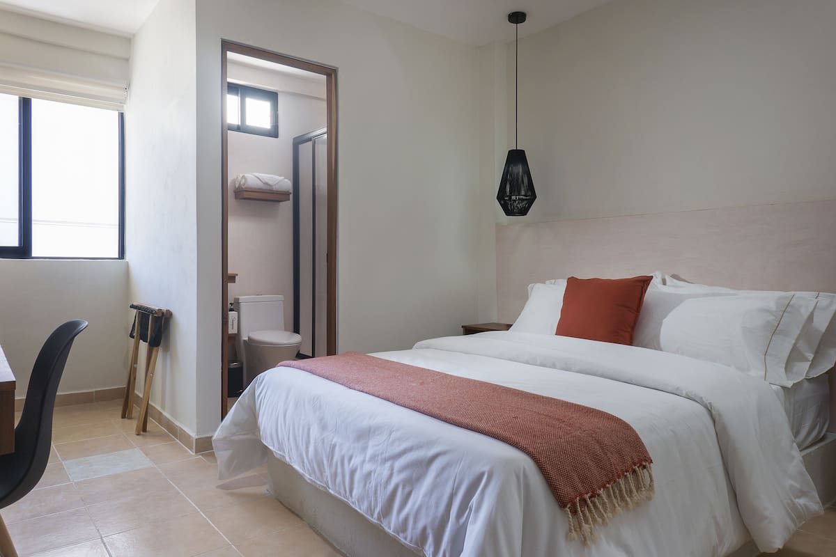 Ein Schlafzimmer mit einem großen Bett, einem Holzstuhl, einem kleinen Tisch und einem Fenster.