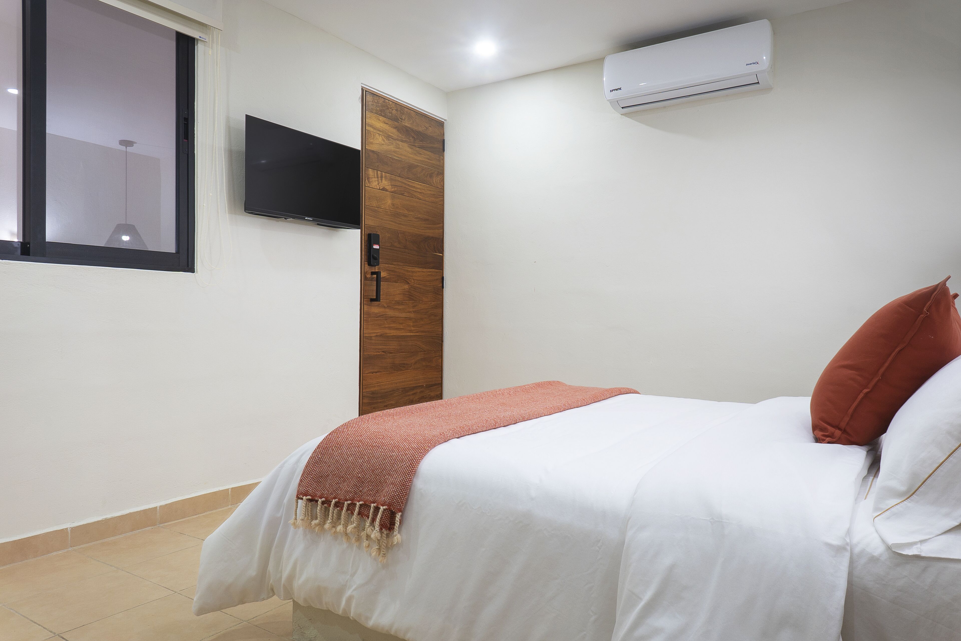 Un dormitorio con cama, televisor montado en la pared, aire acondicionado y ventana.