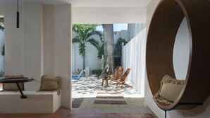 Un intérieur moderne donnant sur un espace piscine extérieur, avec un fauteuil rond en bois et une petite table agrémentée de coussins.