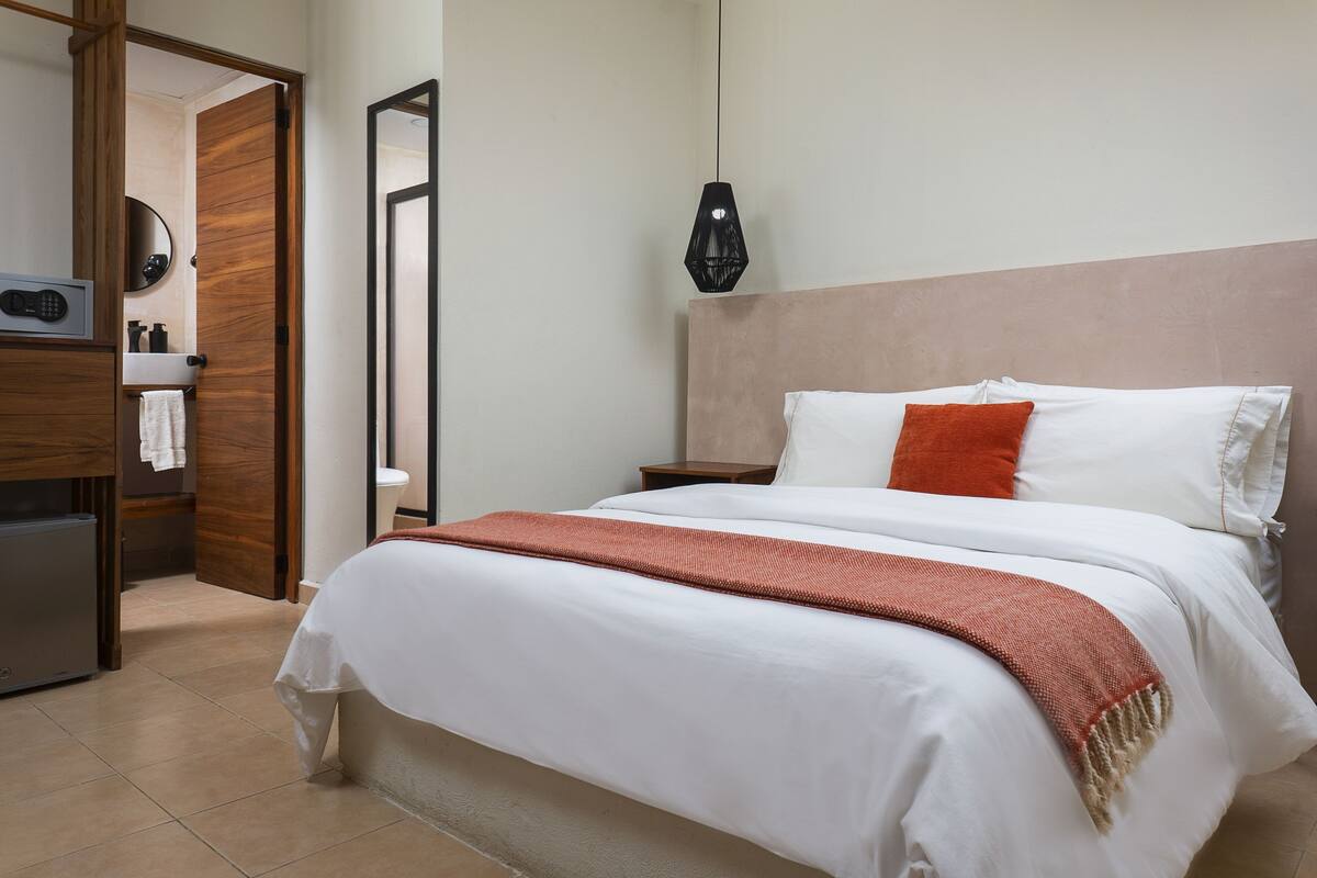 Ein Hotelzimmer mit Bett, Nachttisch, Spiegel, Kleiderschrank und einer Pendelleuchte.