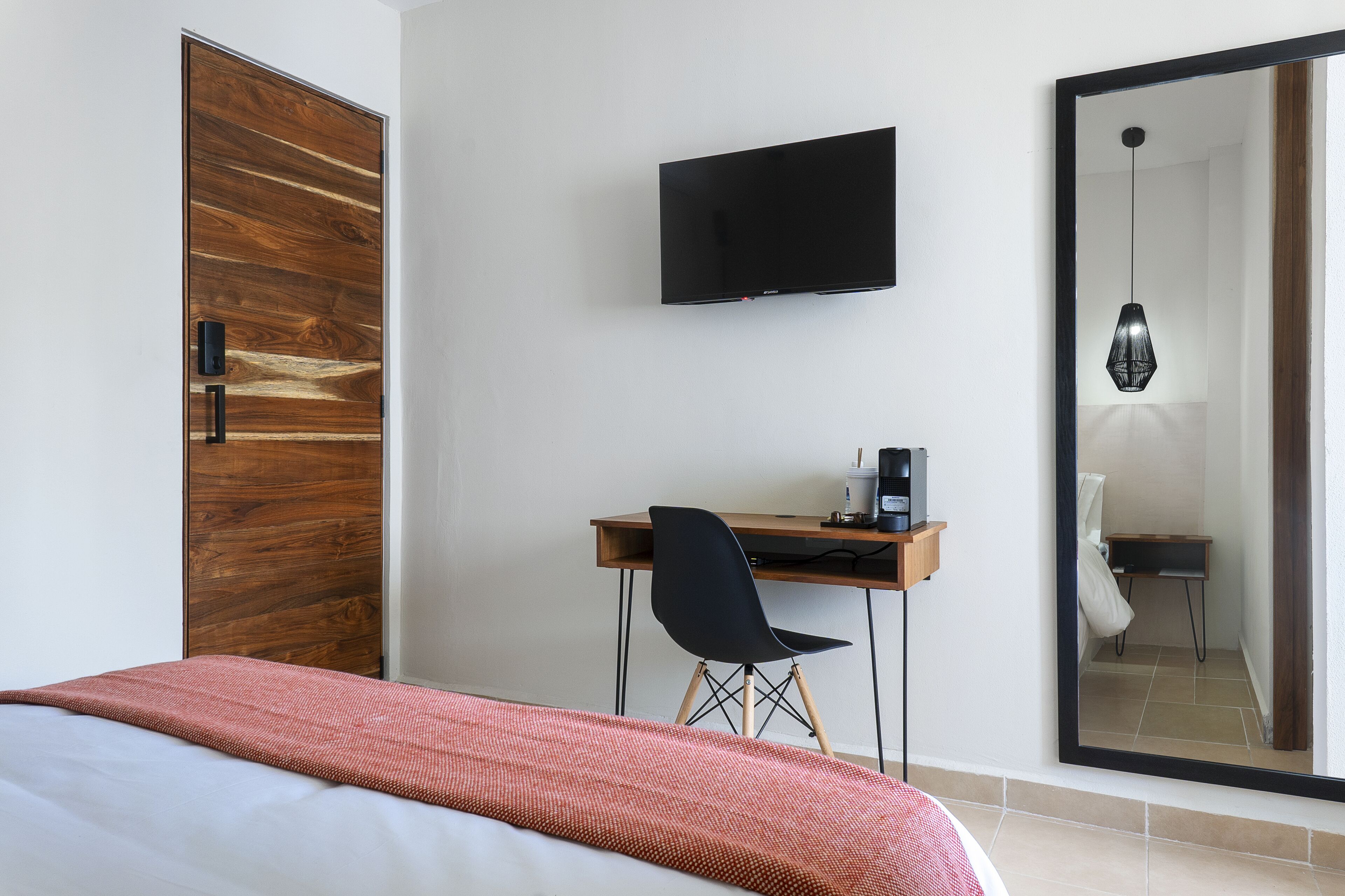 A bedroom with a bed, a desk with a chair, a television, and a large mirror.