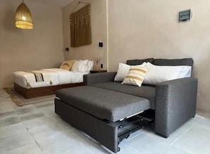 Een kamer met een slaapbank, een apart bed, een kleine tafel en een hanglamp.