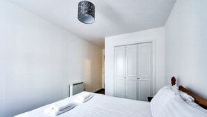 A hotel room with a large bed, a wardrobe, and a radiator. - GuestReady - Spacious 2BR in Leith (Leith)