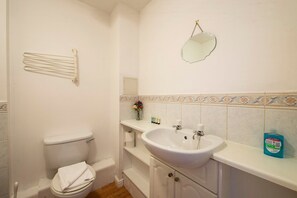 A bathroom with a toilet, sink, and mirror. There is a towel rack above the toilet and a shelf with toiletries. - GuestReady - Spacious 2BR in Leith (Leith)