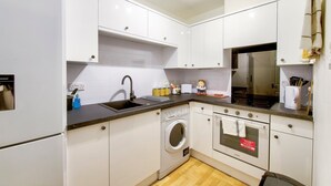 A modern kitchen with white cabinets, a built-in washing machine, and a microwave. - GuestReady - Spacious 2BR in Leith (Leith)