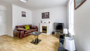 A living room with a brown leather sofa, a fireplace, a television, and a coffee table. - GuestReady - Spacious 2BR in Leith (Leith)