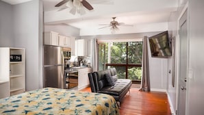 Una habitación compacta con cama, sofá, kitchenette y televisor montado en la pared.
