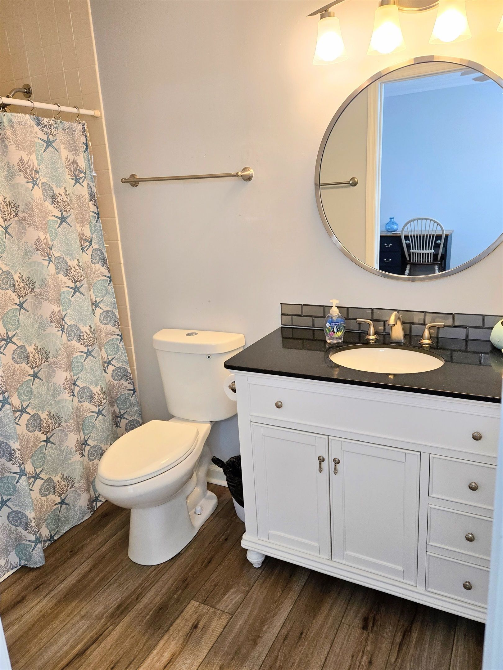 Ein Badezimmer mit einer weißen Toilette, einem Waschtisch mit schwarzer Arbeitsplatte und einem Duschvorhang mit Meeresmotiv.