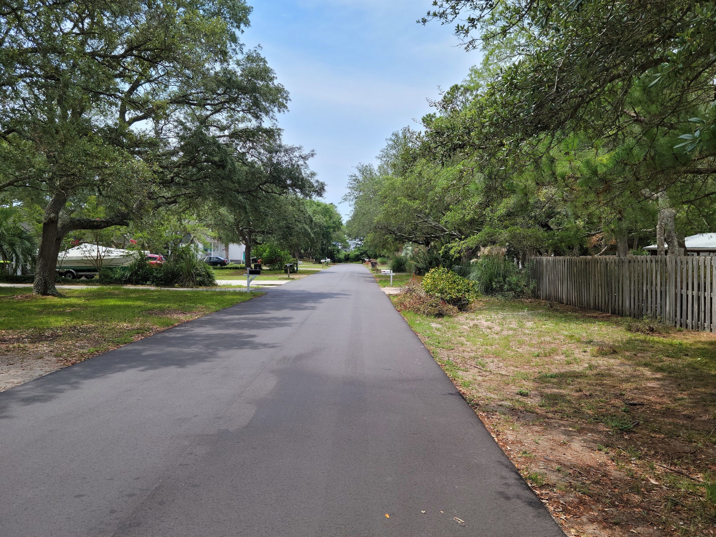 Une rue résidentielle bordée d’arbres et délimitée par une clôture en bois.