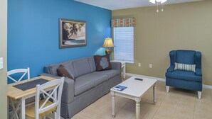 Un salon avec un canapé gris, un fauteuil bleu, une petite table et un tableau accroché au mur.