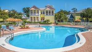 A swimming pool with lounge chairs and a building with a balcony in the background.