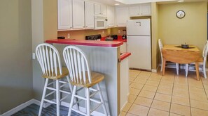 A kitchen with white cabinets, a red countertop, and a dining area with a wooden table and chairs.