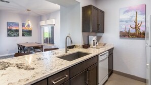 A modern kitchen with a marble countertop, dark cabinetry, and a coffee maker.