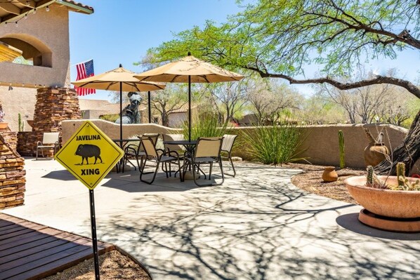 An outdoor patio area with a dining table and chairs, a yellow warning sign, and a cactus planter.