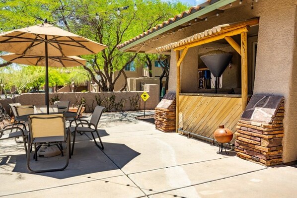 An outdoor patio with a barbecue grill, chairs, and umbrellas.
